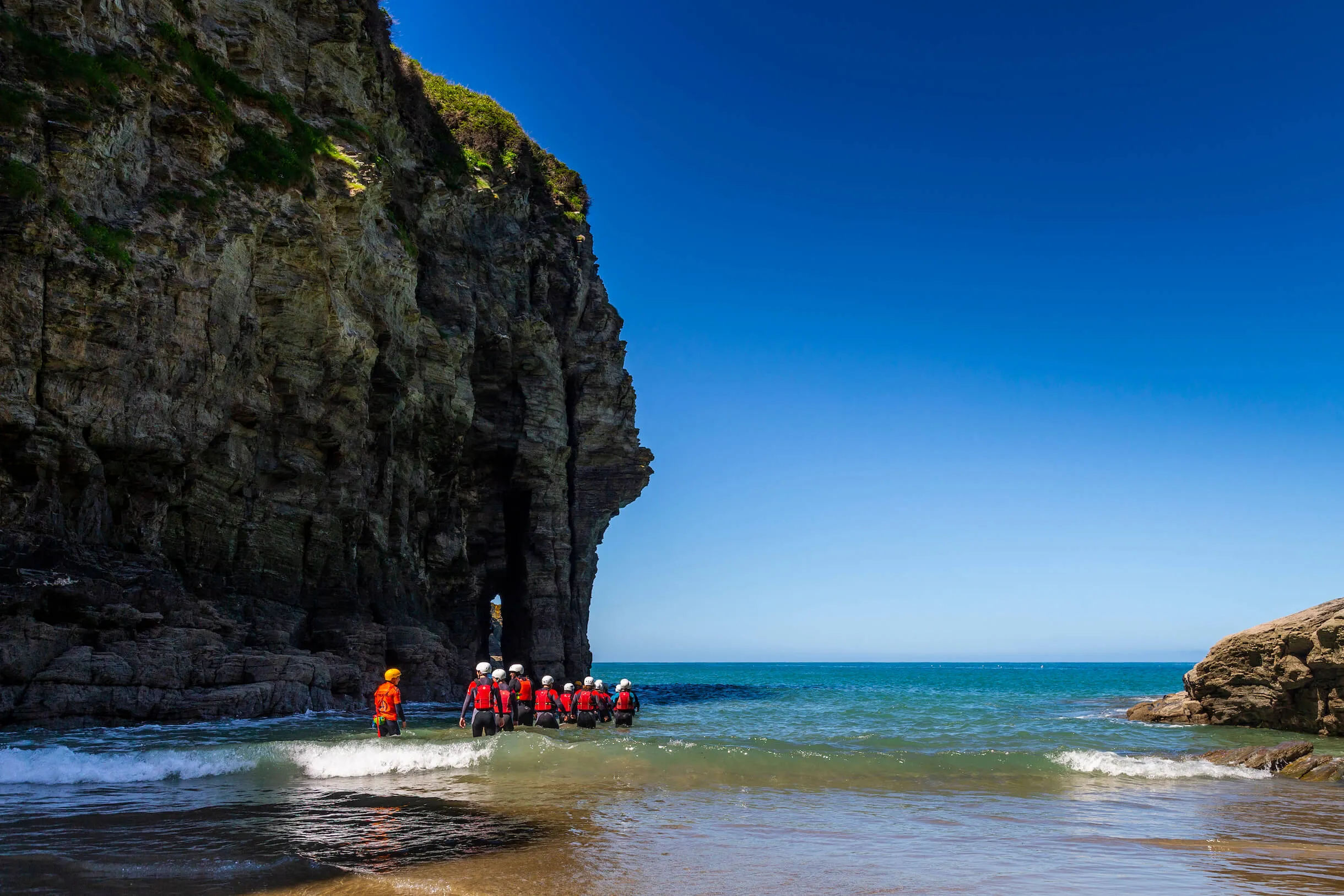 group of people entering the sea in wetsuits, buoyancy aids and helmets at Bossiney Cove