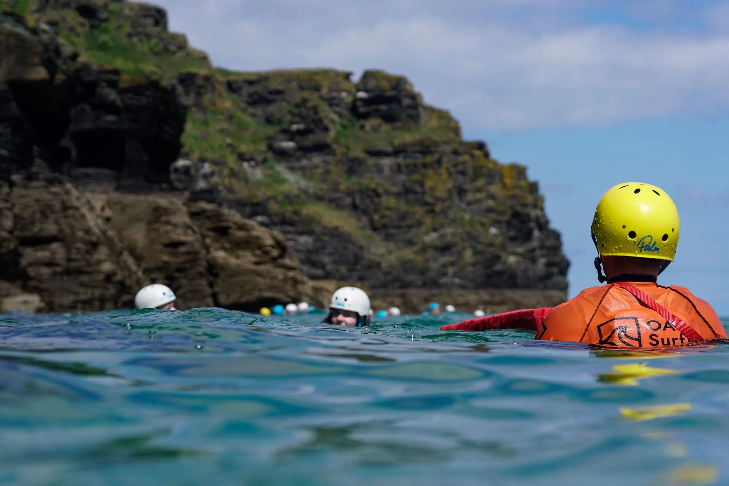 an OA Surf Club coasteer guide watching a coasteering group swim around a headland near Bude, Cornwall