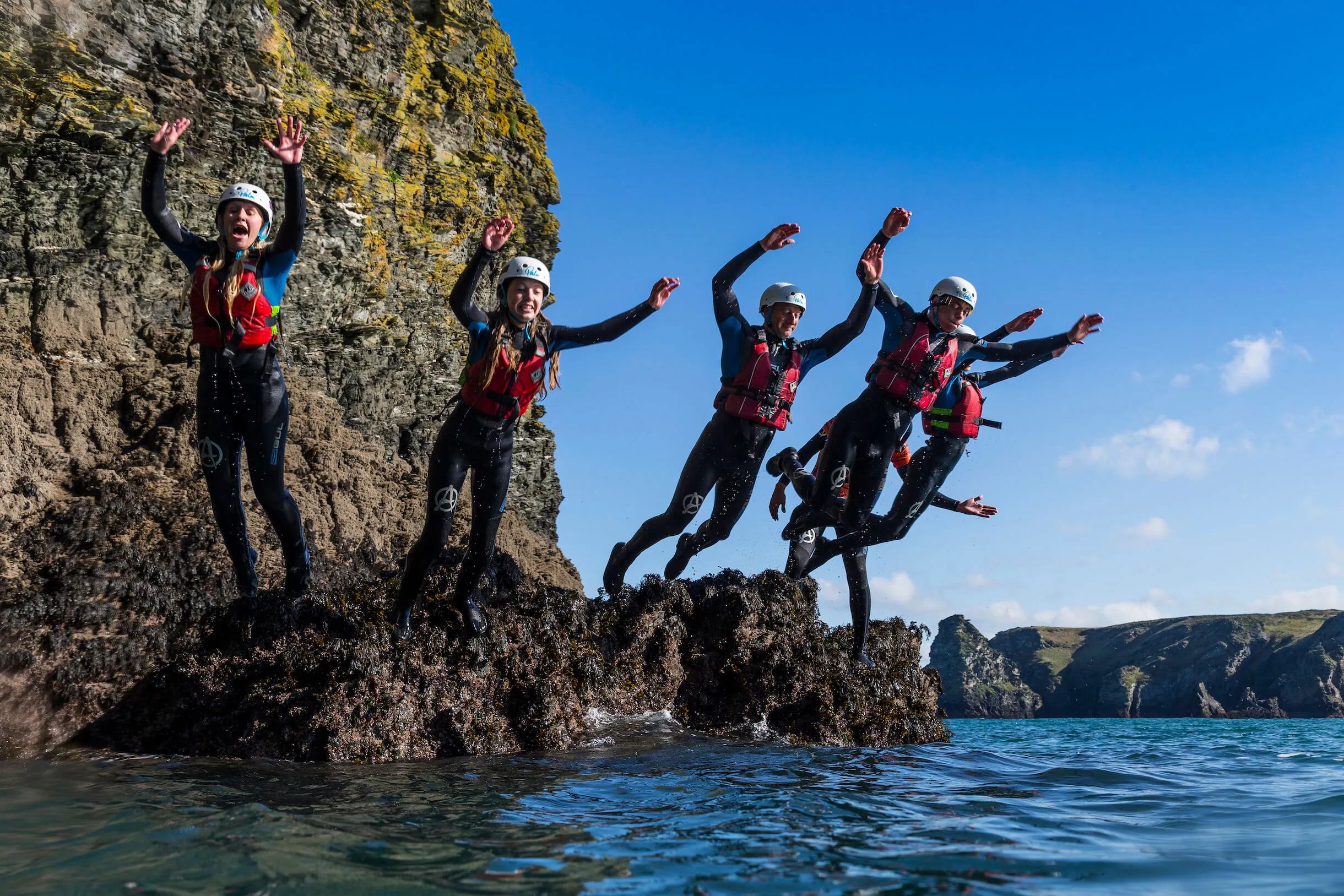 family group jumping off of some rocks while coasteering with OA Surf Club near Bude, Cornwall