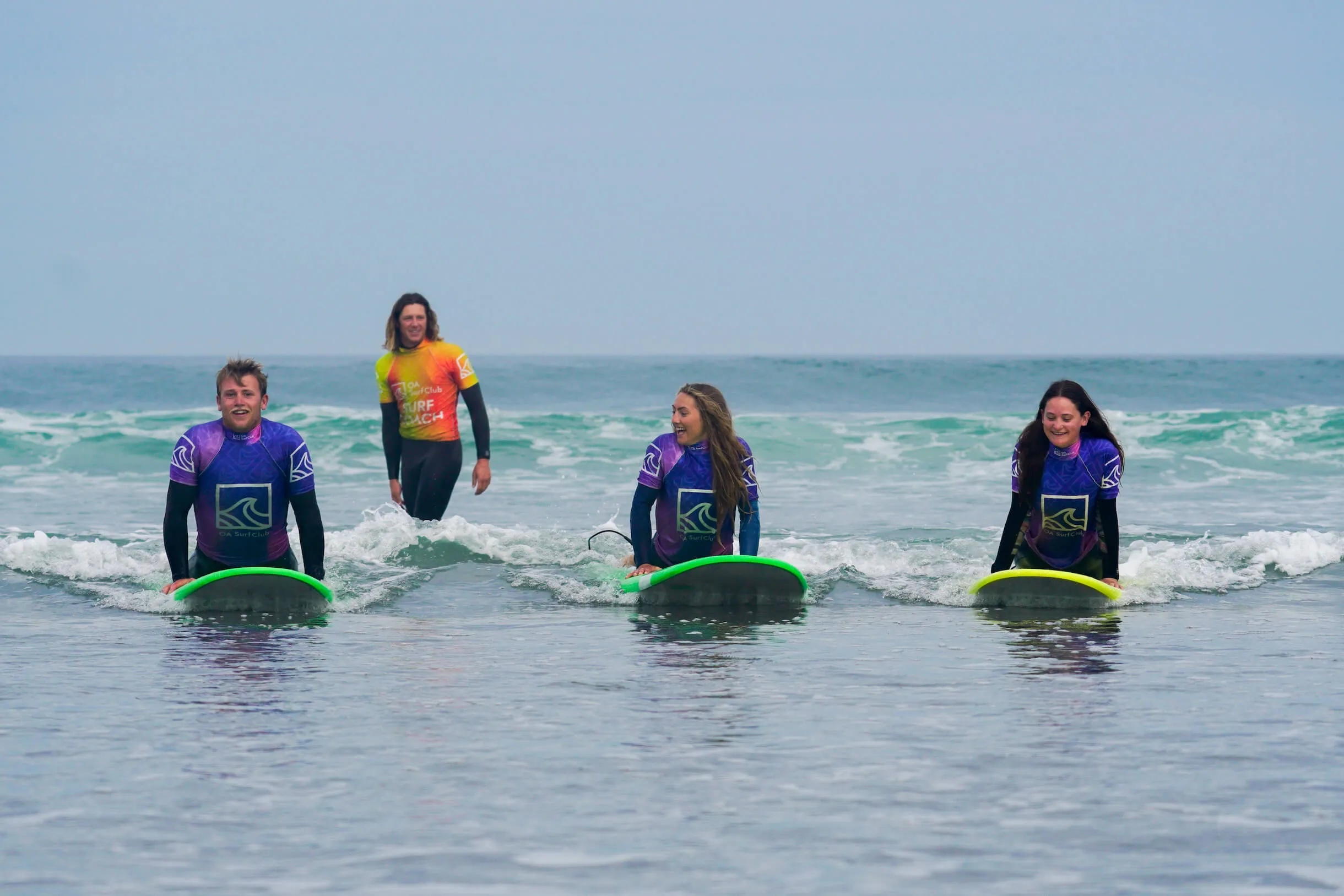 Surfers learning to catch a wave in prone position with a surf coach at Widemouth Bay, Bude