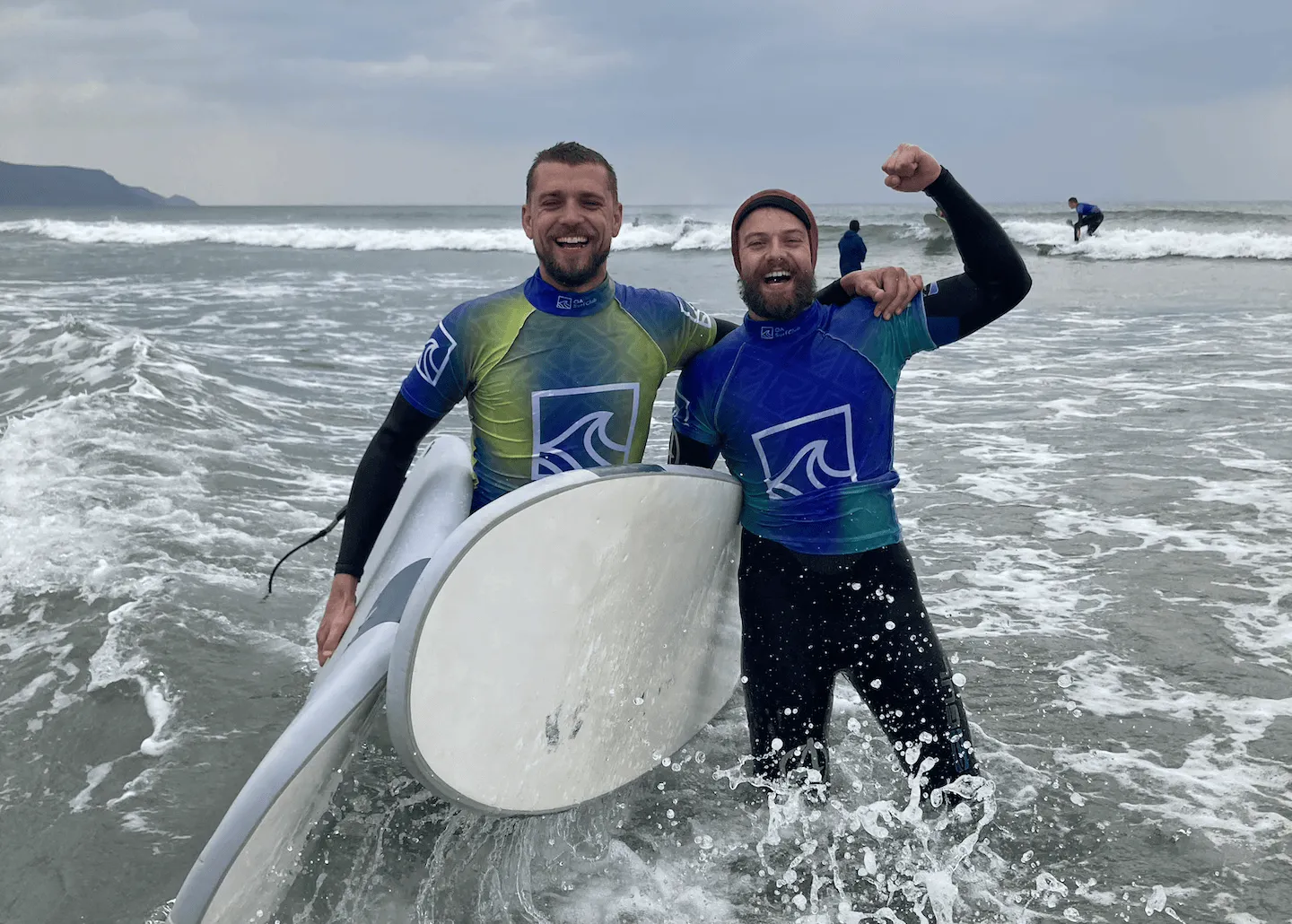 2 people stood in the sea with surfboards at Widemouth Bay after surfing with OA Surf Club